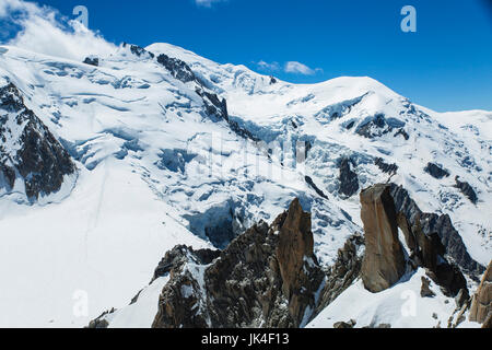 Gli alpinisti salire un alto pinnacolo in pietra circondato da ghiaccio e neve con un ghiacciaio in background sul Mont Blanc Foto Stock