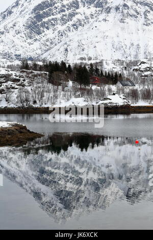 Rosso-bianco cottage in legno sulla penisola Sildpollnes viste attraverso Sildpolltjonna bay. Montaggio Lilandstinden sfondo riflessa sul Austnesfjorden Foto Stock