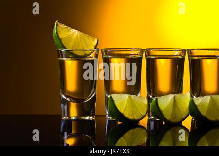 Mexican Gold Tequila in breve i bicchieri con calce su un sfondo riflettente. Foto Stock