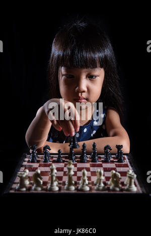 Asian poco ragazza cinese di giocare a scacchi in isolati su sfondo nero Foto Stock