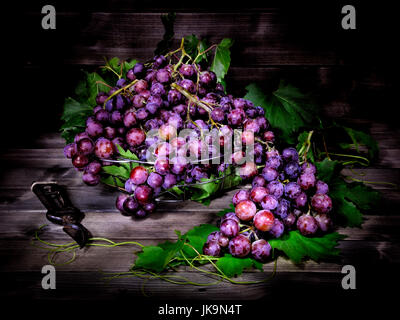 Rosso fresco grappolo di uva giacente su foglie su un vecchio tavolo di legno. Fotografato con luce tecnica di pittura Foto Stock