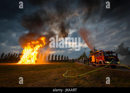 Fire fighter sul motore fire schizza acqua contro le scintille volanti di colonna di fuoco a solstice celebrazioni e festival di mezza estate Foto Stock