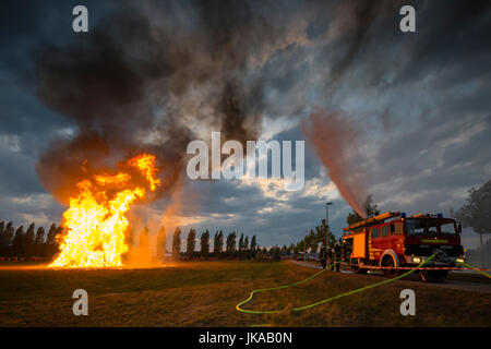 Fire fighter sul motore fire schizza acqua contro le scintille volanti di colonna di fuoco a solstice celebrazioni e festival di mezza estate Foto Stock