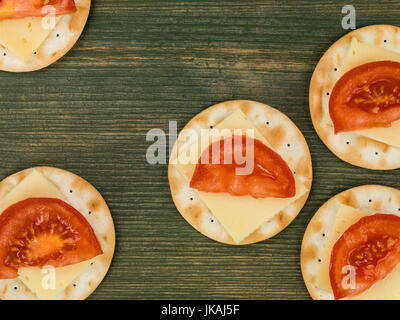 Formaggio e pomodoro su biscotto acqua crackers contro un verde sullo sfondo di legno Foto Stock