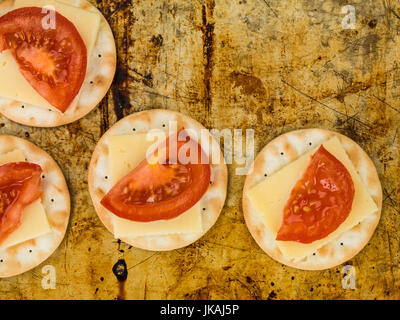 Formaggio e pomodoro su biscotto acqua crackers contro un usato distressed forno Foto Stock