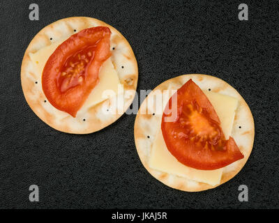 Formaggio e pomodoro su biscotto acqua crackers contro uno sfondo nero Foto Stock