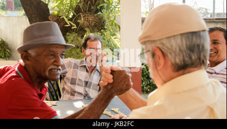 Felice active pensionati, old ispanica uomini senior del divertimento e del gioco di domino a casa. Buddies celebrando la vittoria e il tifo Foto Stock
