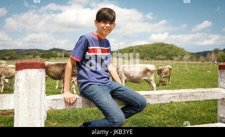 La vita quotidiana per il giovane agricoltore con le mucche in campagna. I contadini lavorano in Sud America con bestiame nel paese della famiglia ranch. Bambino felice smilin Foto Stock
