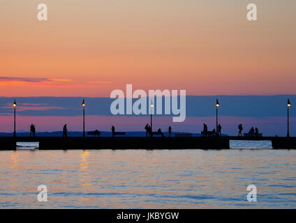 Sagome umane camminando sul dock al tramonto Foto Stock