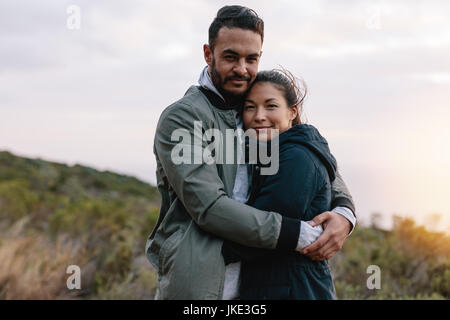 Ritratto di una coppia romantica abbracciando in campagna. Bel giovane che abbraccia la sua ragazza asiatica. Foto Stock