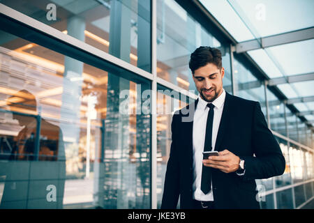 Imprenditore utilizza lo smartphone e sorridente in aeroporto. Young business executive con telefono cellulare all'aeroporto. Foto Stock