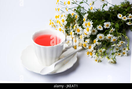 I fiori di camomilla e una tazza di tè su bianco Foto Stock