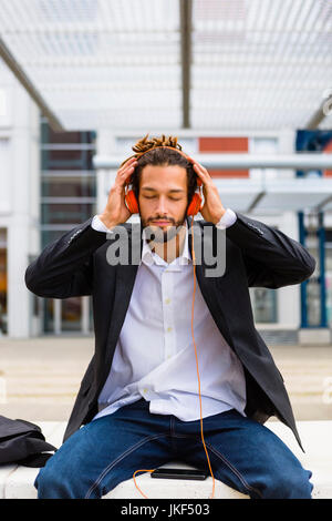 L'Italia, Firenze, giovane imprenditore con dreadlocks ascoltare musica in città Foto Stock