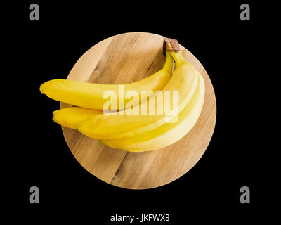 Quattro delle banane gialle su una tavola di legno e isolate su uno sfondo nero. Foto Stock