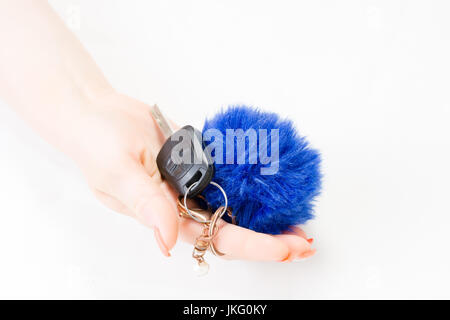 Una donna di mano trattiene le chiavi dell'auto e sportello elettronico sbloccare con un blu soffici portachiavi a sfera isolata su sfondo bianco. Chiodo con arte Foto Stock