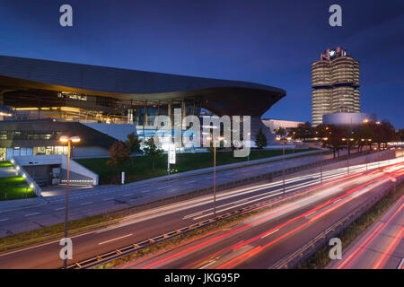 In Germania, in Baviera, Monaco di Baviera, BMW Welt azienda showroom, BMW la sede centrale della società e il museo BMW con traffico di sera Foto Stock