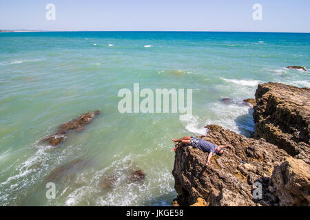 Giovane uomo disteso sulle rocce scogliere sull'oceano di Algarve Portogallo Foto Stock