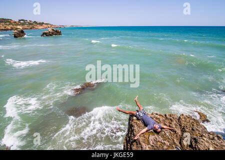 Giovane uomo disteso sulle rocce scogliere sull'oceano di Algarve Portogallo Foto Stock