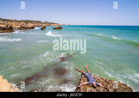 Giovane uomo disteso sulle rocce scogliere sull'oceano di Algarve Portogallo Foto Stock