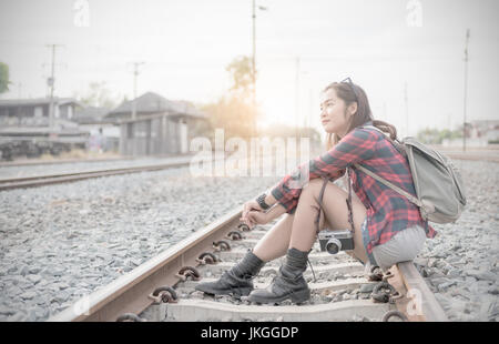 Hipster ragazza giovane aspettando il treno sulla Ferrovia e di sfondo tono vintage, concetto viaggi e tempo libero Foto Stock