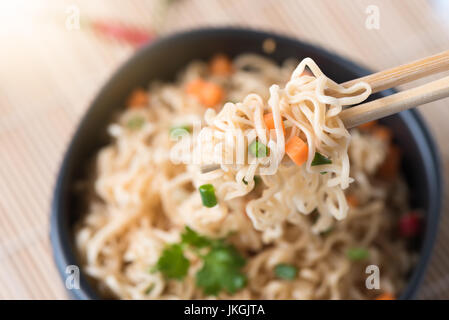 Chiuso fino tagliatelle istante con verdure su chopstick, cibo spazzatura o fast food concept. Foto Stock