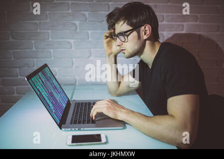 Giovane uomo programer lavorare sul computer portatile nella notte e hack la rete. Giovani attacco hacker una rete nella notte. Hacker Foto Stock