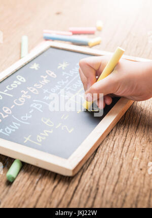Poco la scrittura a mano su una lavagna completamento di equazioni matematiche su uno sfondo di legno Foto Stock