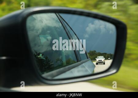 Guardando fuori lato passeggero Specchio retrovisore in corrispondenza di un carrello che ci seguono come alberi di sfocatura sulla Florida Turnpike voce a nord-ovest verso Orlando, Florida Foto Stock