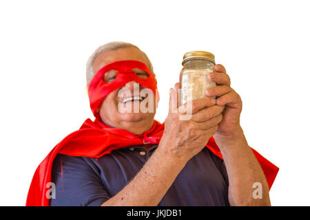 Felice uomo maturo in costume da supereroe tenendo un denaro il vasetto di vetro riempito con euro isolati su sfondo bianco, il concetto è quello degli anziani è ancora energia Foto Stock