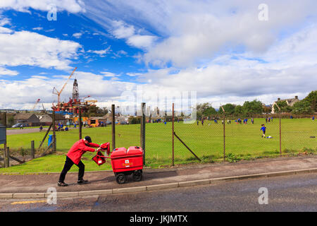 Invergordon, Scozia: portalettere / supporto per posta il passaggio di recinzione di scuola parco giochi. Piattaforma di perforazione in background. Foto Stock