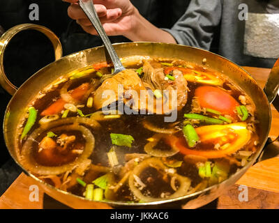 Autentica tradizionale tailandese alle erbe soup food in ottone hot pot: calda e acida zuppa di maiale in una pentola bollente, Tom Yum zuppa di maiale, Tomyam Moo Toon. Foto Stock