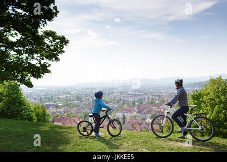 Madre e figlio in bicicletta al castello con vista panoramica sulla città vecchia di Lubiana, Slovenia. Foto Stock