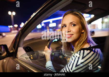 Bella giovane donna alla guida la sua macchina di notte. Foto Stock