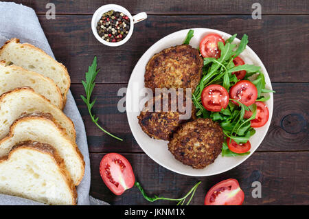 Succose bistecche su una piastra con una insalata di pomodoro e rucola su legno scuro dello sfondo. Vista dall'alto. Foto Stock