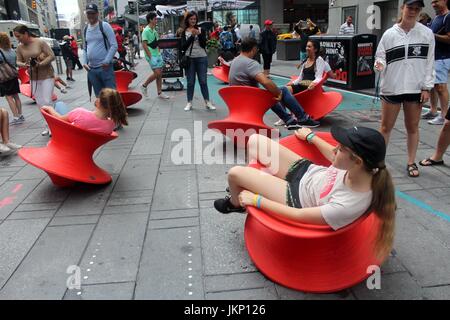 New York, US. Il 24 luglio, 2017. New York, NY, USA. -- 24 luglio, 2017-- i giovani e i giovani di cuore i visitatori a Times Square si fermò un momento di divertimento a mezzogiorno con il Magis Spun sedia. Il montante filate sedie è un affascinante sedia che assomiglia più ad un recipiente scultoreo di un sedile. Ma quando si appoggia sul suo lato, si forma una confortevole sedia funzionale che consente di roccia da lato a lato o girare intorno a. Credito: G. Ronald Lopez /DigiPixsAgain.us/Alamy Live News Foto Stock