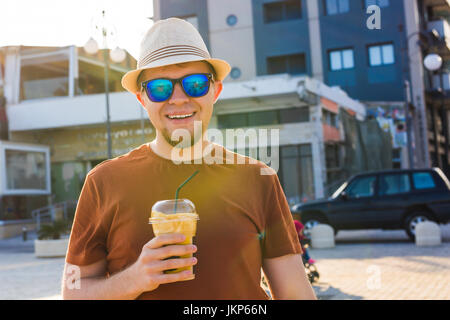 Ritratto di Allegro attraente barbuto hipster giovane uomo beve caffè ghiacciato o frappe all'aperto Foto Stock