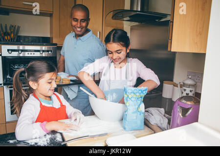 Padre rendendo biscotti con le sue due figlie nella cucina di casa propria. Foto Stock