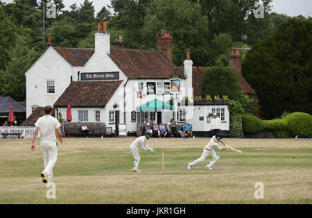 Gli spettatori seduti fuori l'Orzo Mow pub godendo di un villaggio partita di cricket tra Tilford e Grayswood suonata in Tilford verde in Waverley, Surrey. Foto Stock