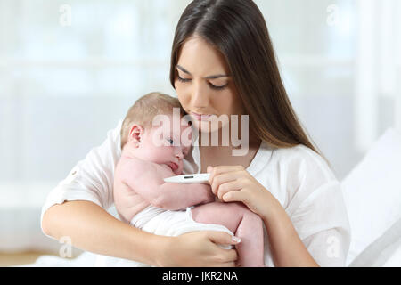 Madre usando un termometro th, controllare la temperatura del suo bambino malato a casa Foto Stock