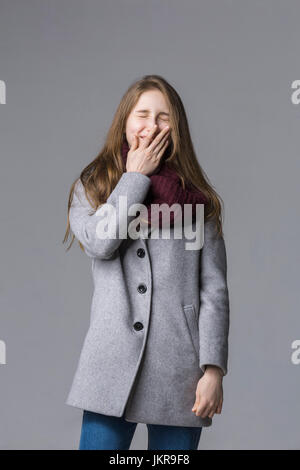 Sorridente ragazza adolescente che copre la bocca in piedi contro lo sfondo grigio Foto Stock