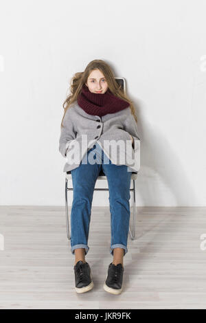 Ritratto di ragazza adolescente sdraiata su sedia contro il muro bianco Foto Stock
