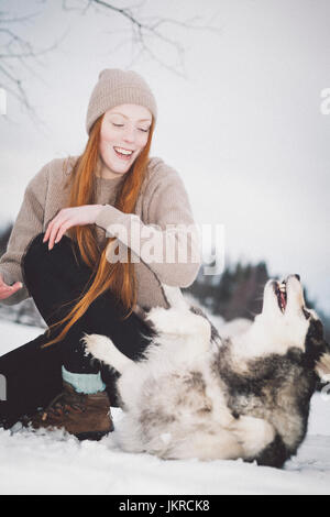 Allegro giovane donna giocando con Siberian Husky sul campo nevoso