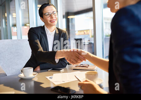 Ritratto di certi leader femmina sorridente felicemente agitando la mano di un irriconoscibile business partner durante la riunione di lavoro in cafe Foto Stock