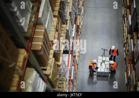 Al di sopra di vista delle persone che lavorano in grandi magazzini, contando le merci sul carrello in movimento tra gli scaffali con scatole confezionate Foto Stock