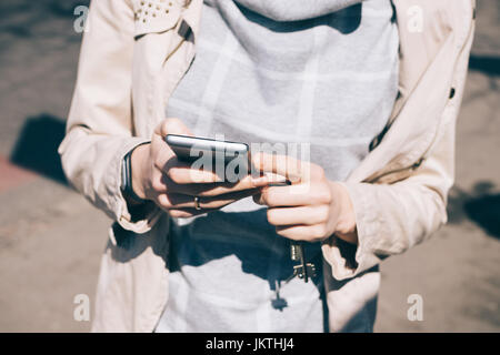 Giovane donna in una giacca beige possiede un telefono cellulare, close-up Foto Stock