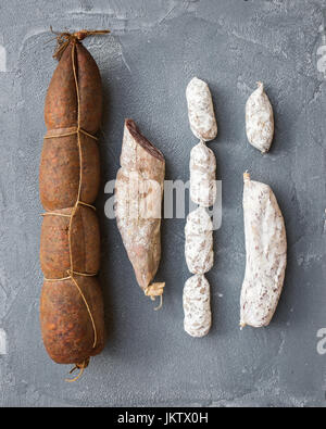Salame salsicce di vario tipo su una ruvida grigio sfondo concreto Foto Stock