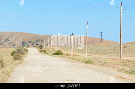 La vecchia strada nella regione arida con pali di calcestruzzo per l'energia elettrica lungo il cordolo. Penisola di Crimea Foto Stock