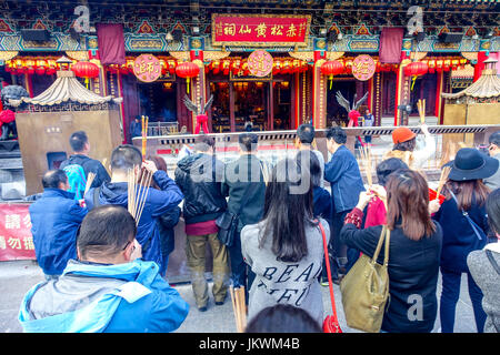 HONG KONG, CINA - 22 gennaio 2017: la folla di persone in possesso di una loro mani un bastoncini di incenso e di pregare all'interno di Wong Tai Sin tempio buddista a pra Foto Stock