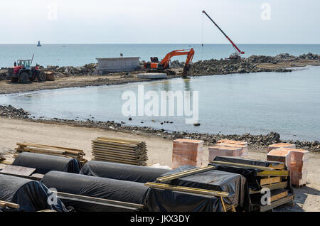 Gru escavatore e costruzione nuova banchina in mare con materiali da costruzione nelle vicinanze Foto Stock