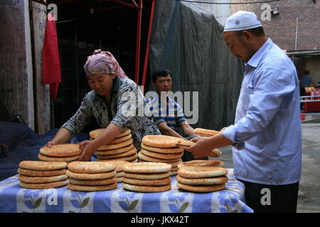 La donna che porta una pila di pane pita in vendita nella città vecchia Urumqi Foto Stock